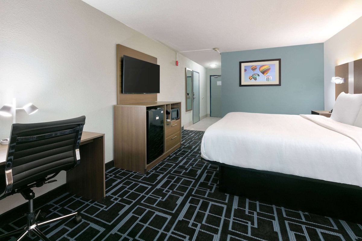A hotel room with a bed, desk, chair, TV, wardrobe, and a framed picture on the wall.