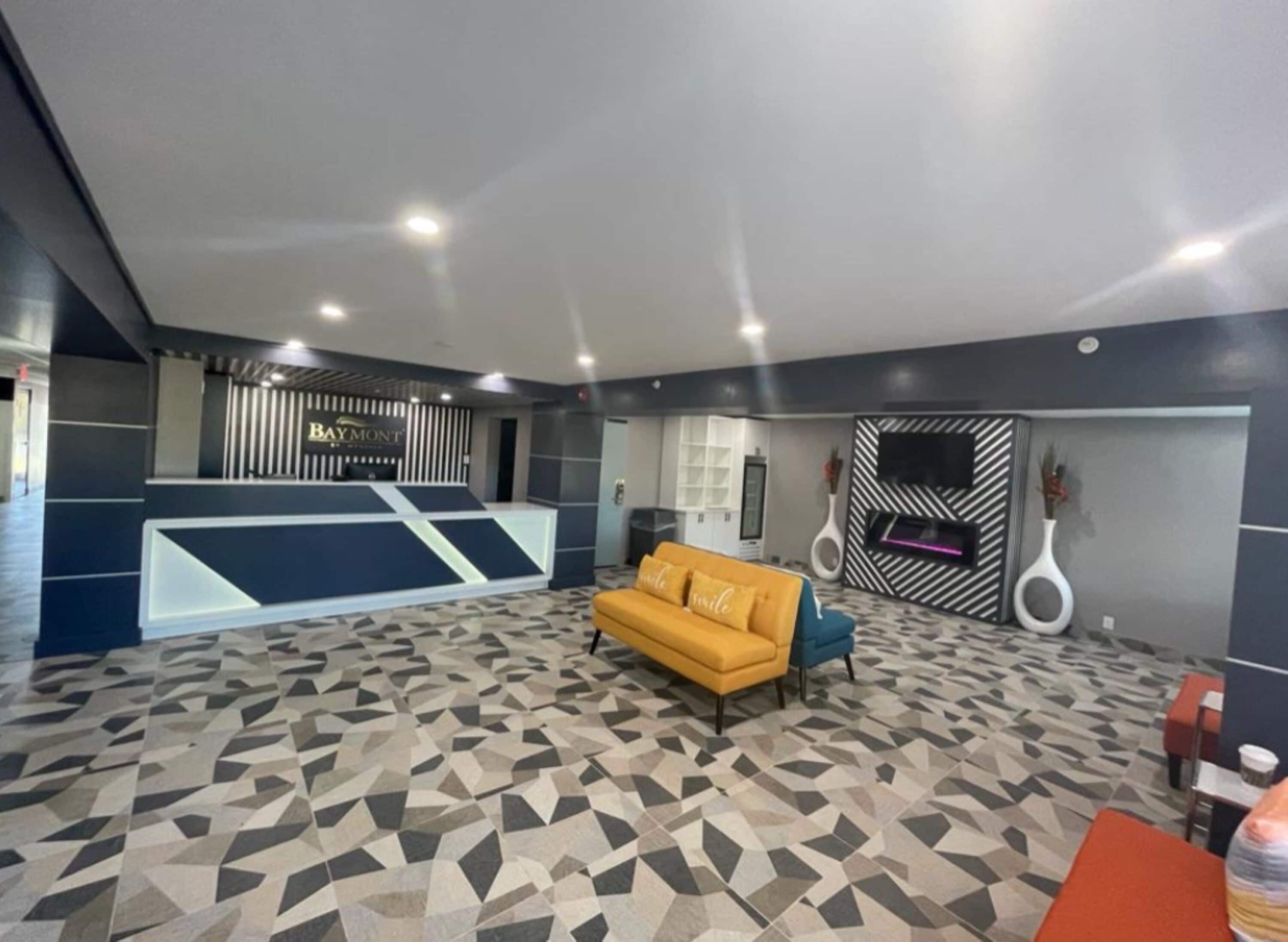 A modern hotel lobby with a reception desk, a yellow sofa, and a patterned floor.