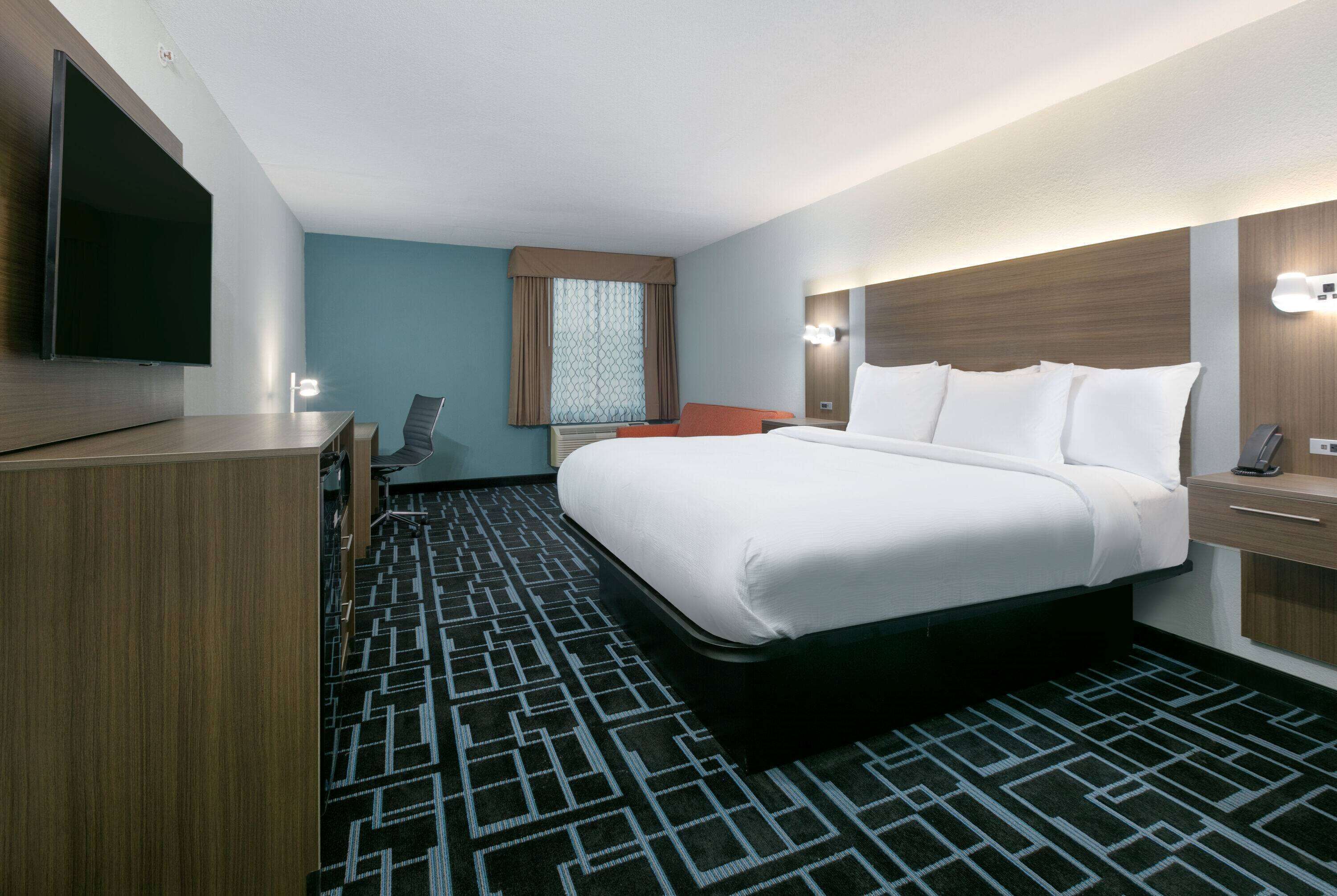 A hotel room with a large bed, a flat-screen TV, a desk, and a chair.
