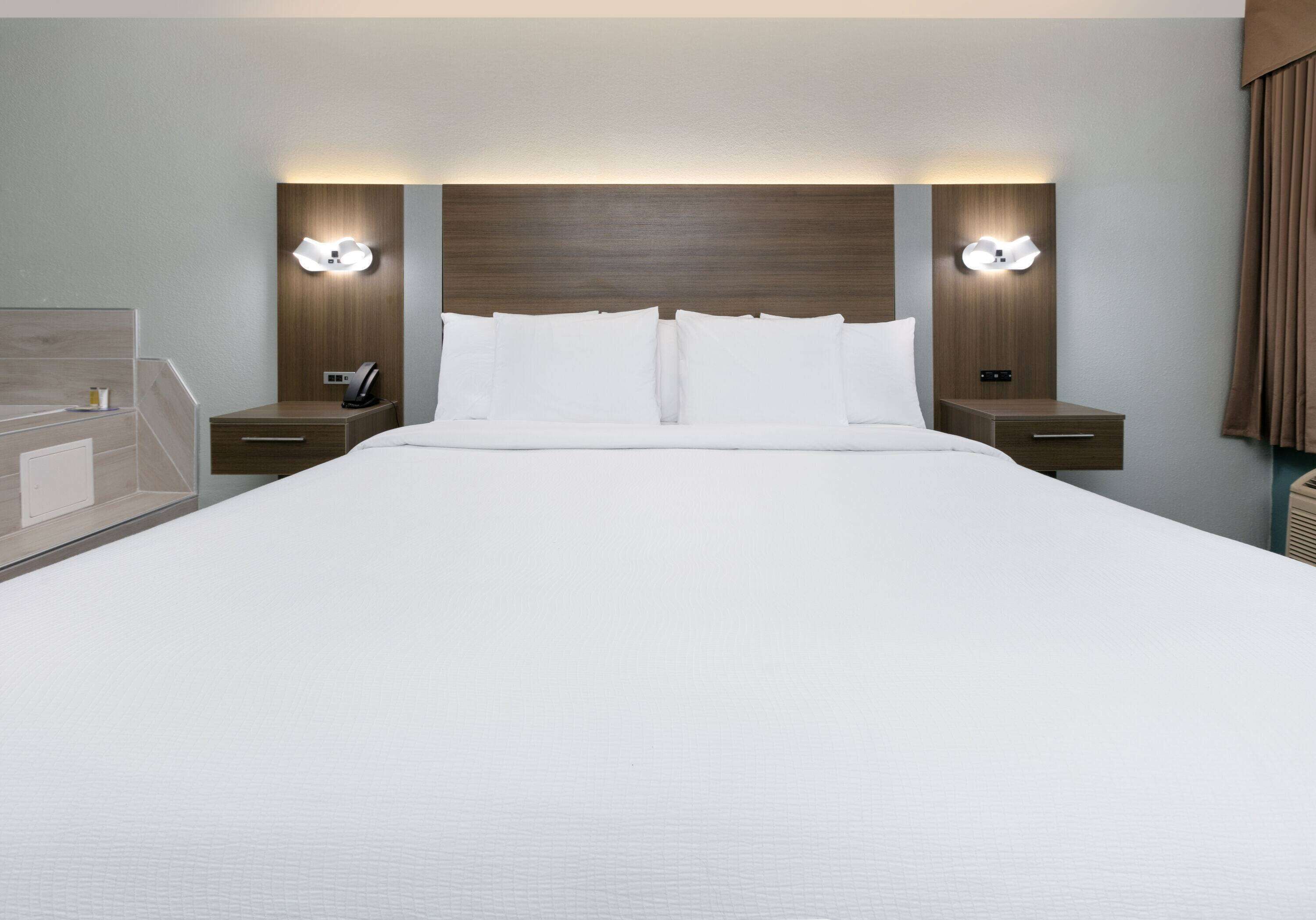 Une chambre d’hôtel avec un grand lit, deux tables de chevet avec des lampes et une tête de lit dotée d’un éclairage intégré.