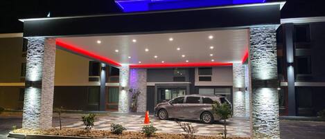 A modern hotel entrance with a covered parking area, stone pillars, and a car parked inside.