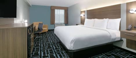 A hotel room with a large bed, a desk, a chair, a TV, and a window with curtains.