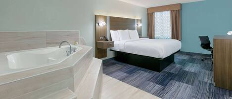 A modern hotel room with a large bathtub, a bed with white linens, a desk, and a chair.