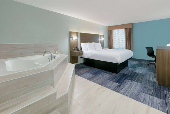 Una habitación de hotel moderna con una bañera grande, una cama con ropa blanca, un escritorio y una silla.