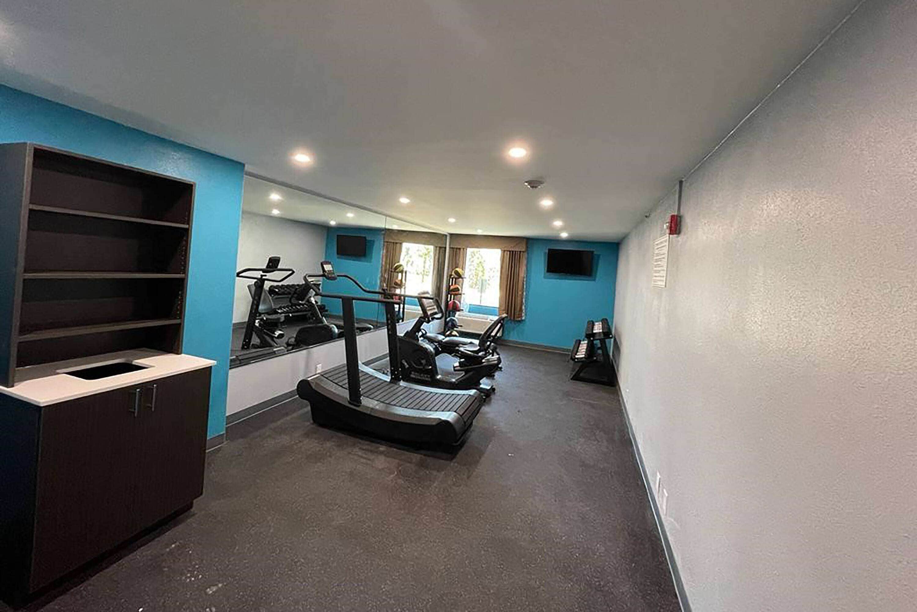 A gym with treadmills, elliptical machines, and a mirrored wall.