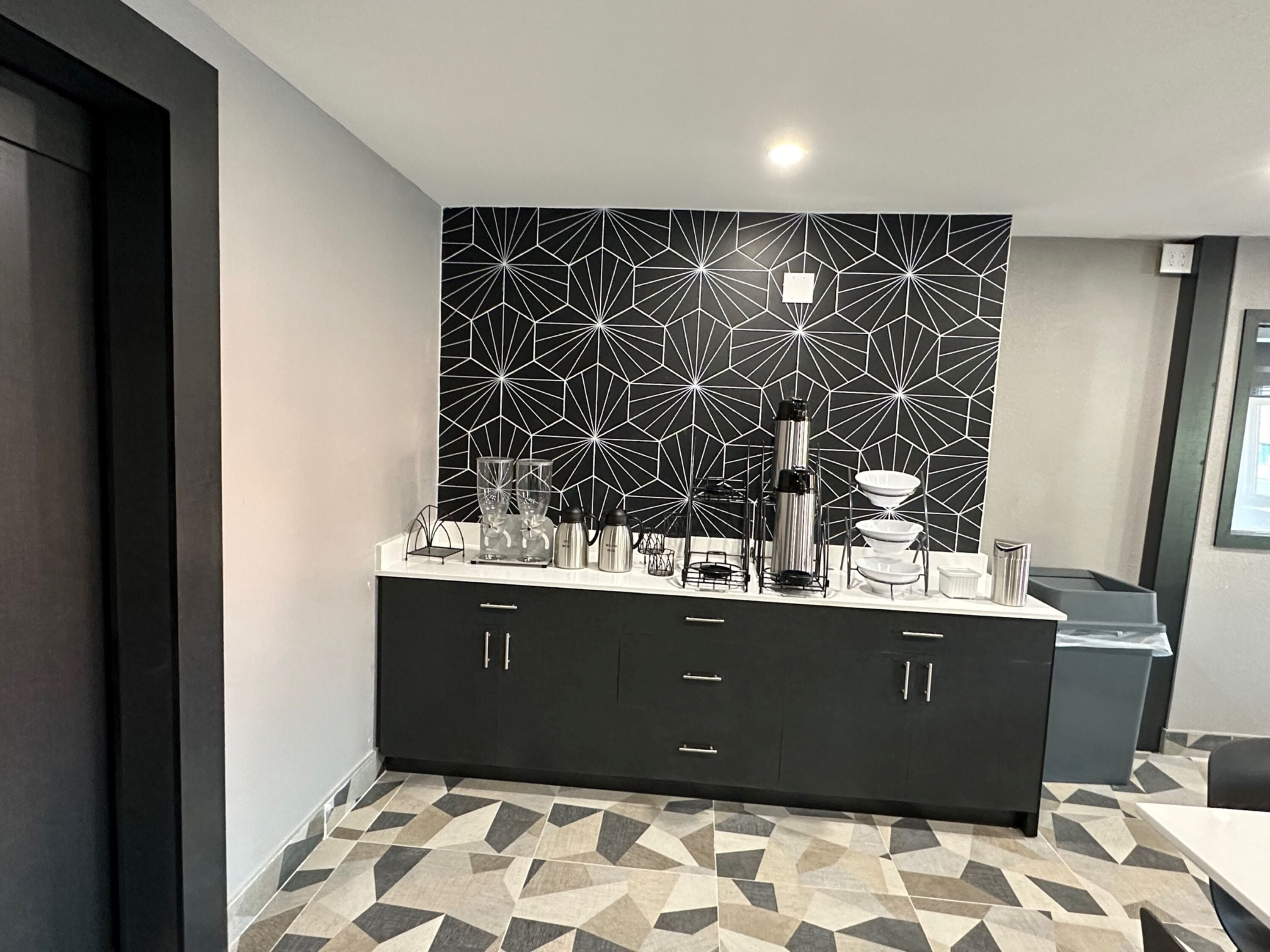 A modern kitchen with a geometric backsplash, a black cabinet with drawers, and a tiled floor.