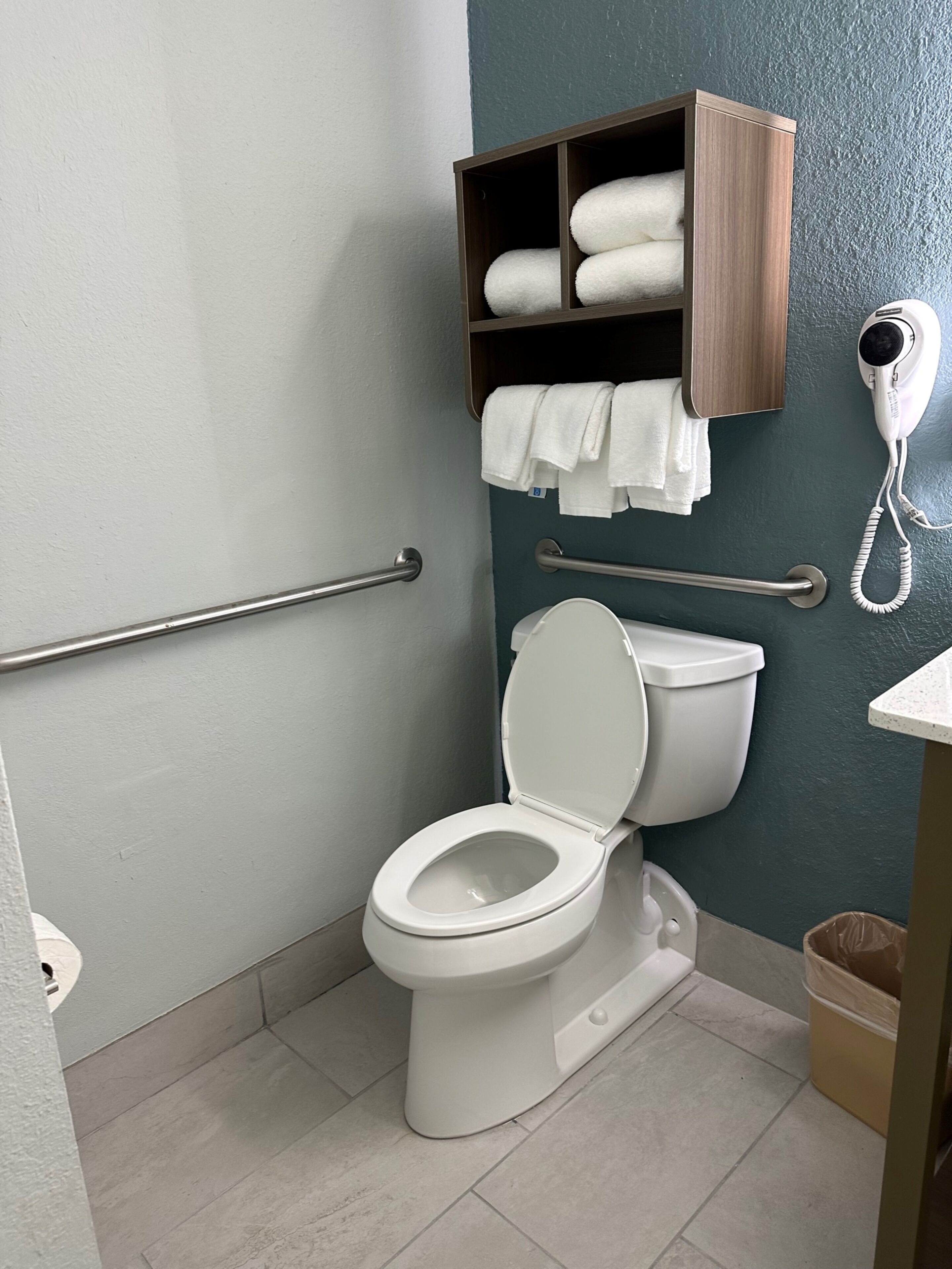Een moderne badkamer met een wit toilet, een houten plankje met handdoeken en een haardroger.