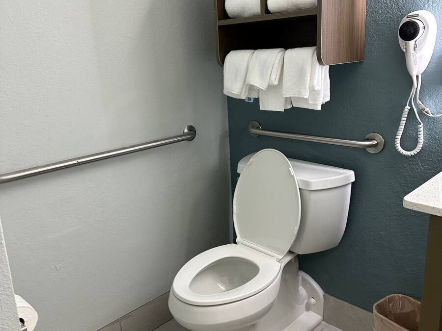 Een moderne badkamer met een wit toilet, een houten plankje met handdoeken en een haardroger.