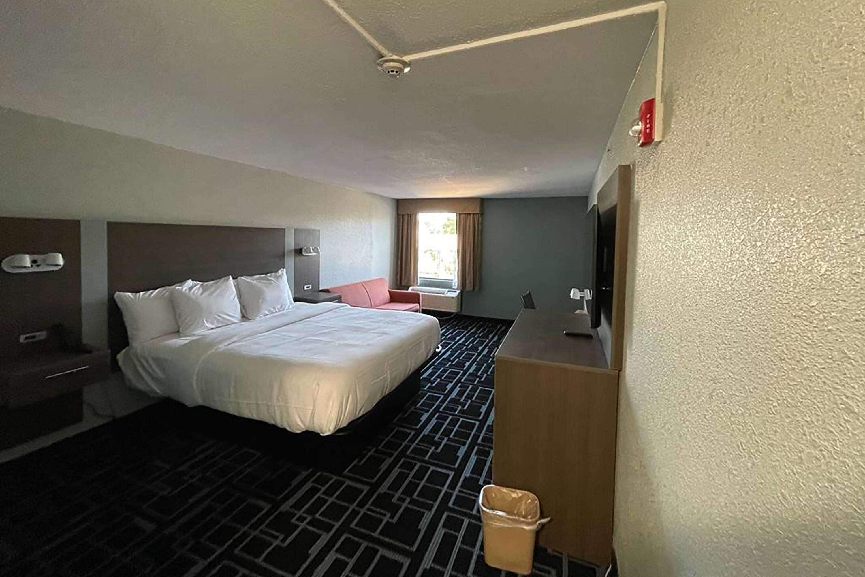 A hotel room with a large bed, a desk, a chair, and a window with curtains.