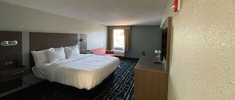 A hotel room with a large bed, a desk, a chair, and a window with curtains.