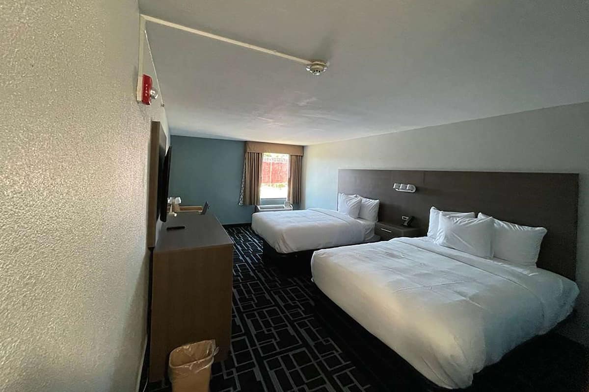 A hotel room with two beds, a desk, and a window with curtains.