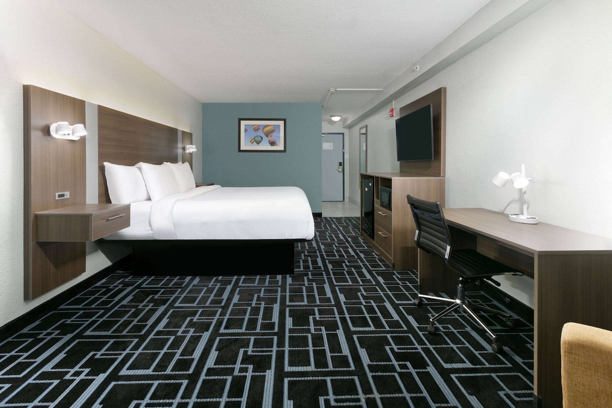 A hotel room with a bed, desk, chair, and a television.