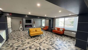 En modern entréhall med ett golv i geometriskt mönster, en gul soffa, orange fåtöljer och en accentvägg i svart och vitt.