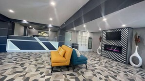 En modern entréhall med en receptionsdisk, två soffor, en platt-TV och ett golv med geometriskt mönster.