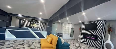 Egy modern előtér, amelyben található egy recepciós pult, két kanapé, egy síkképernyős televízió és geometrikus mintázatú padlóburkolat.