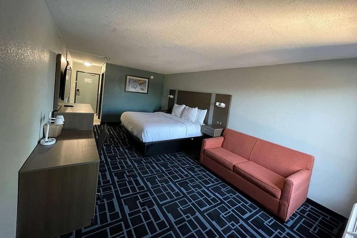A hotel room with a bed, a red sofa, a desk, and a patterned carpet.