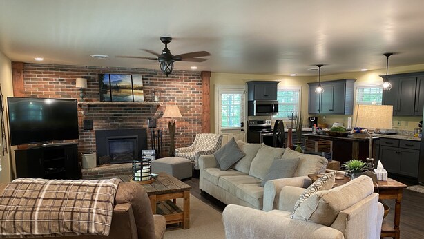 A living room with a fireplace, a television, and a kitchen area with cabinets and appliances. - Enjoy Nature In Style! (Jamestown)