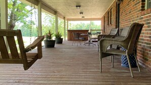 A covered outdoor patio with wooden flooring, wicker furniture, and potted plants. - Enjoy Nature In Style! (Jamestown)