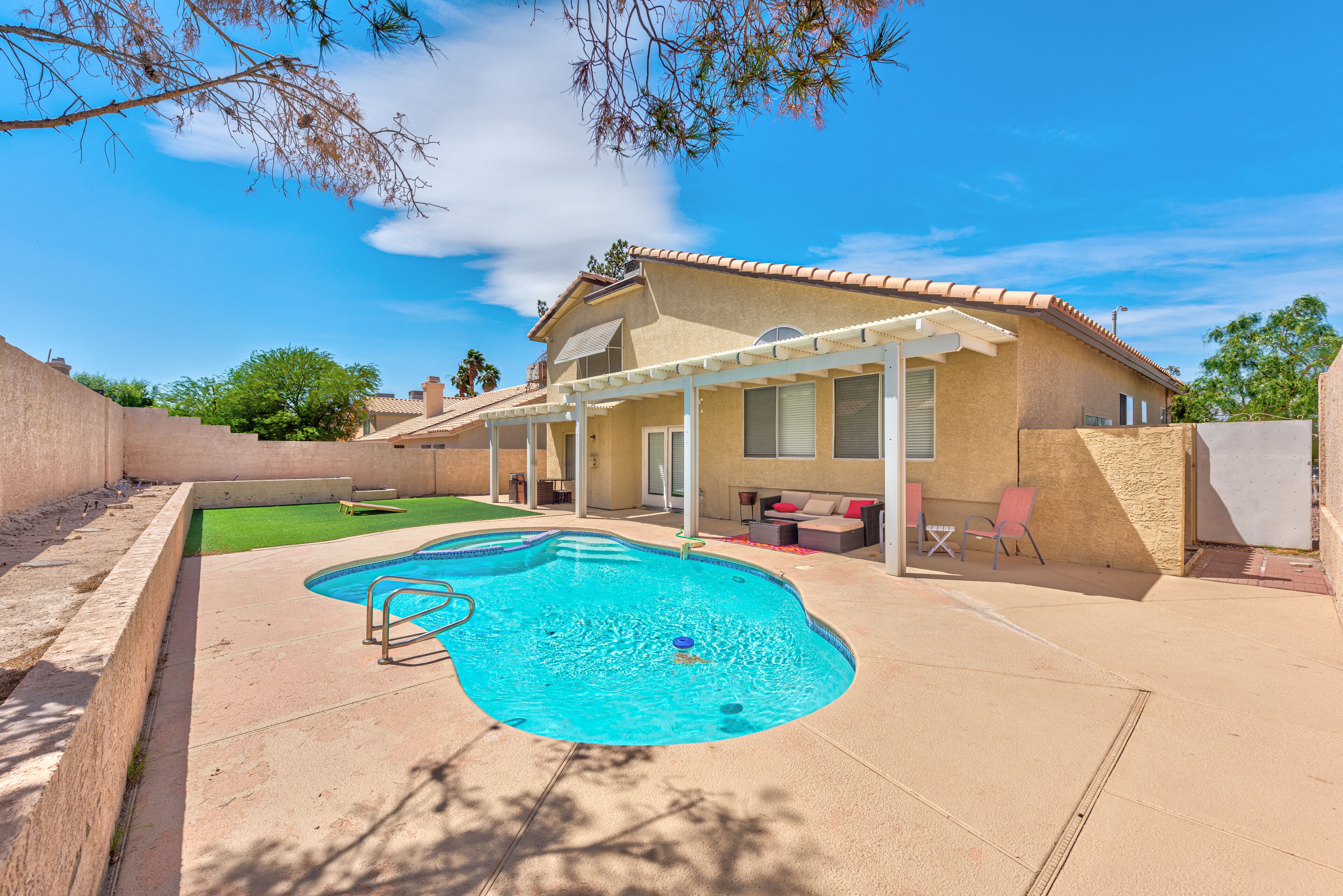 A backyard with a swimming pool, a covered patio, and a house with a tiled roof.