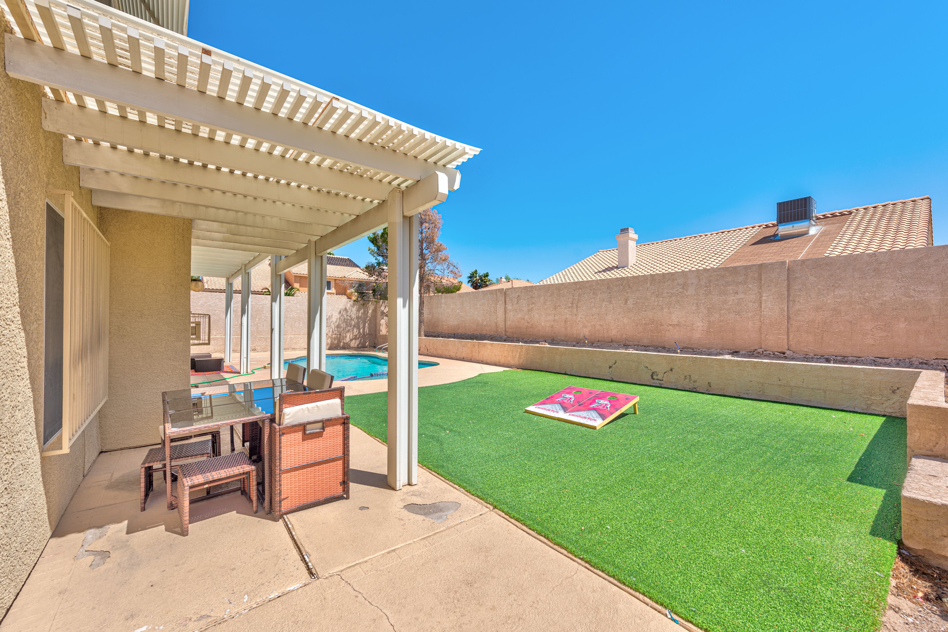 A patio with a pergola, a pool, and artificial grass.