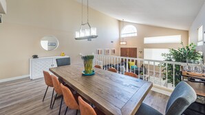 A spacious dining area with a wooden table, orange chairs, and a hanging light fixture.