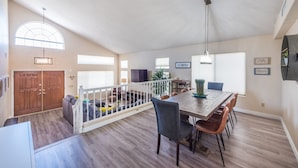 A spacious living area with a wooden dining table, chairs, and a staircase leading to an upper level.