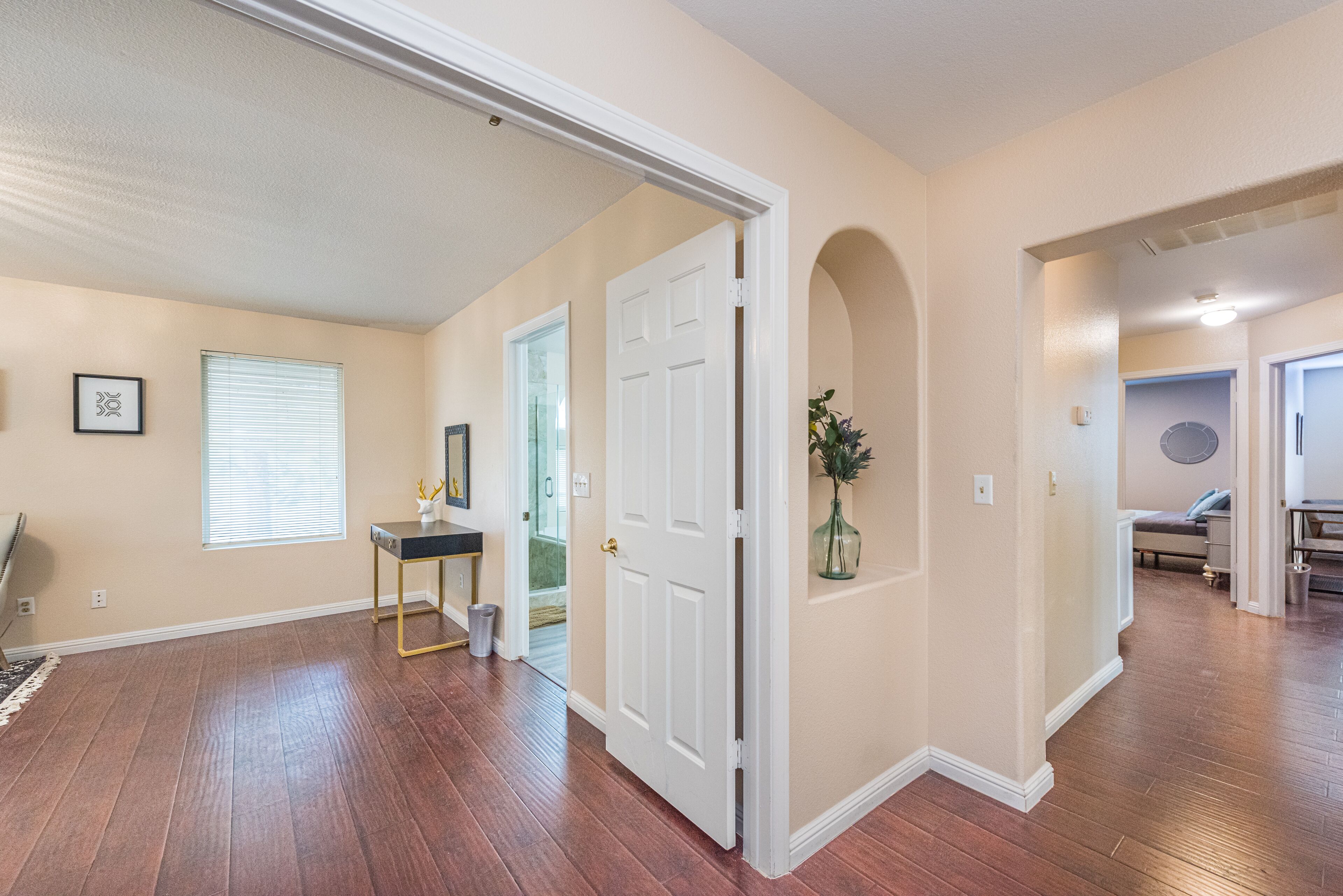 A spacious hallway with hardwood flooring, a white door, and a small desk with a chair.
