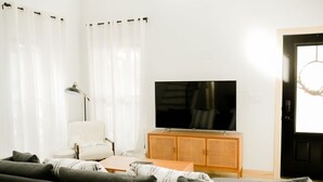Ein Wohnzimmer mit einer Couch, einem Fernseher auf einem Holzschrank, einer Lampe und einer Tür mit einem Kranz.