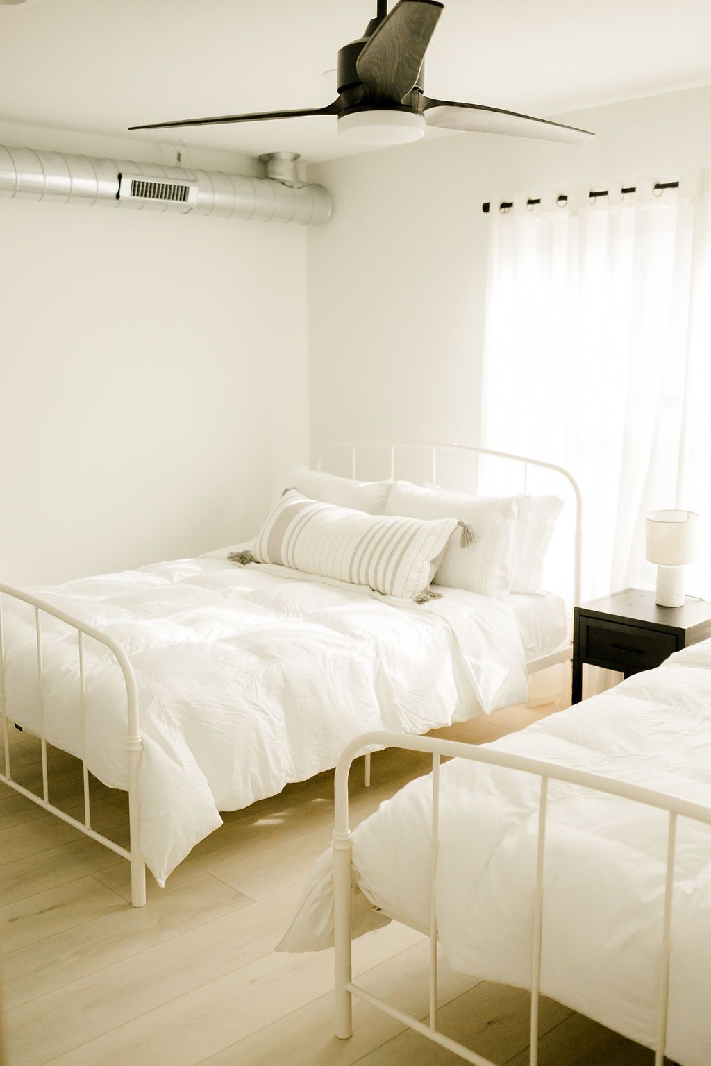 Een slaapkamer met twee bedden, een plafondventilator en een raam met gordijnen.