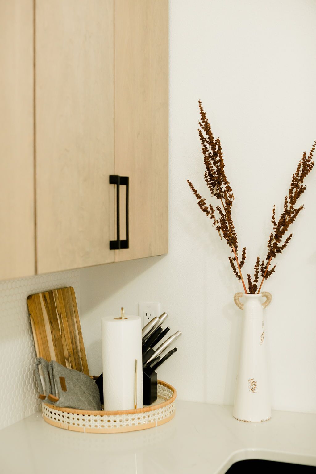 A kitchen counter with a white vase containing dried plants, a white candle, and kitchen utensils.