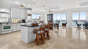 A spacious kitchen with white cabinetry, a large island with bar stools, and a view of the ocean through large windows. - Exclusive Private Residence on the Gulf of Mexico, a Premier Vacation Retreat (Sarasota)