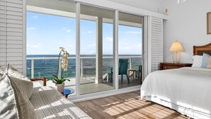 A bedroom with a large sliding glass door leading to a balcony with a view of the ocean. There is a bed with white bedding, a nightstand with a lamp, and a potted plant. - Exclusive Private Residence on the Gulf of Mexico, a Premier Vacation Retreat (Sarasota)