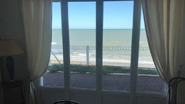 A room with a large window overlooking a beach, a chair, and a lamp. - Feet in the water  (Langrune-sur-Mer)