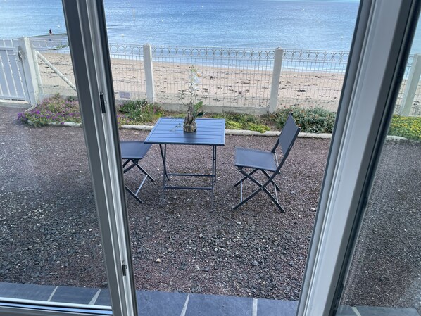 A patio with a table and chairs, a decorative plant, and a view of the beach and ocean.
