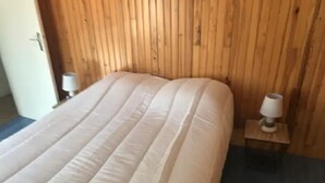 A room with a wooden headboard, a bed with a white mattress, and a small bedside table with a lamp. - Feet in the water  (Langrune-sur-Mer)