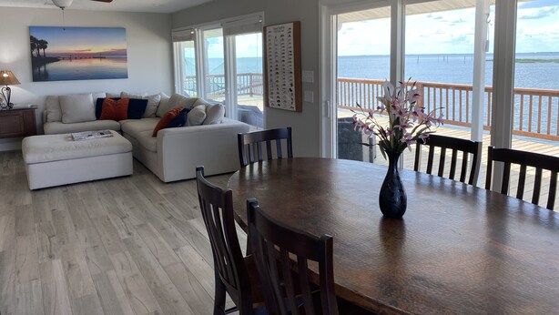 Uma sala de estar ampla, com uma grande mesa de jantar, assentos confortáveis e vista para o oceano.