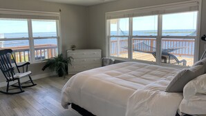 Quarto com uma cama grande, duas janelas com vista para a praia, uma cadeira de balanço e um armário.