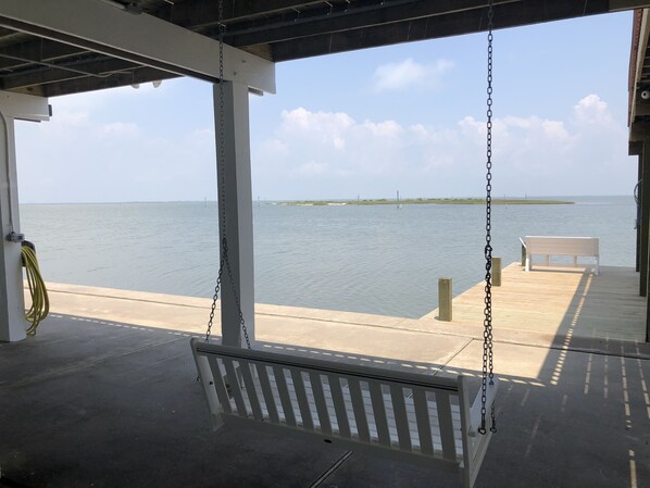 A covered deck with a swing, a bench, and a view of the water.