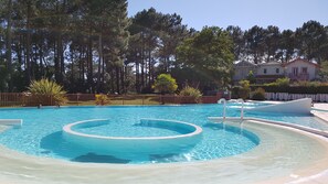 Ein Pool mit einer kreisförmigen Wasserspüle, umgeben von einem Zaun, Bäumen und einem Gebäude im Hintergrund.
