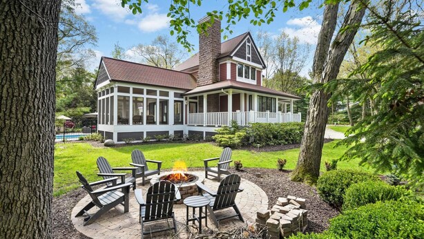 Una casa de dos pisos con un porche cubierto, un brasero y sillas Adirondack.