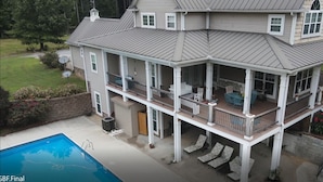 Ein zweistöckiges Haus mit einer großen Terrasse, einem Schwimmbad und einem überdachten Patio.