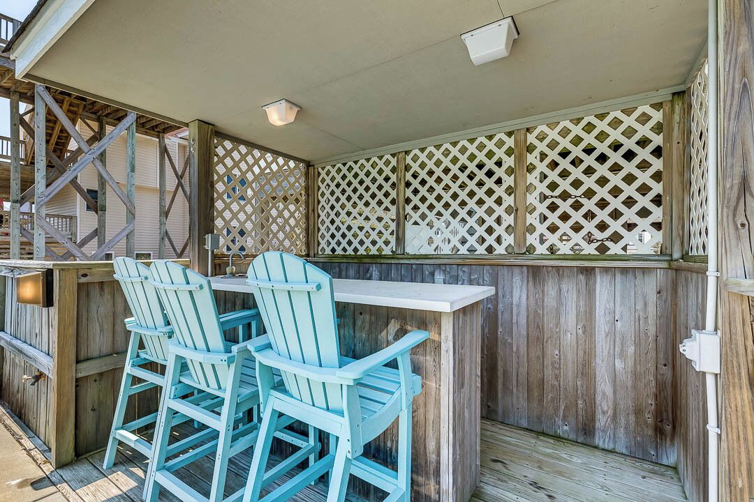 An outdoor patio with wooden lattice panels, a white table, and blue Adirondack chairs.