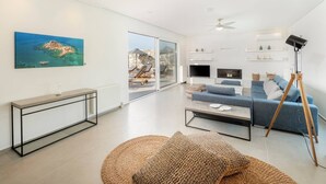 Un salon moderne avec une grande fenêtre, un canapé bleu, une table basse et un téléviseur.