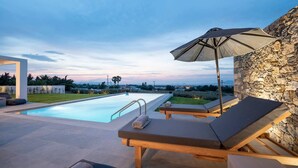 Un espace piscine extérieur moderne, doté de chaises longues et d’un parasol, entouré de murs en pierre et offrant une vue sur le paysage.
