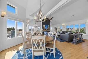 A spacious living area with a dining table, chairs, and a large window overlooking a cityscape.