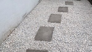 Ein Innenhof mit weißer Mauer, einem Metallzaun und einem Kiesweg.