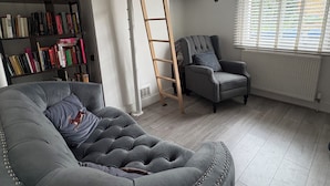 Ein Wohnzimmer mit einem grauen Sofa, einem grauen Sessel, einem Bücherregal und einer an der Wand angelehnten Leiter.