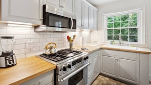 A kitchen with white cabinets, a stainless steel stove, a microwave, and a window with a view of greenery.