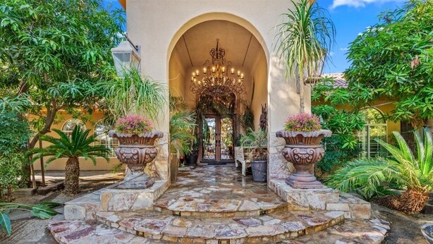 A stone staircase leading to an arched entrance with a chandelier, surrounded by potted plants and tropical foliage. - HUGE LUX Estate, Pool/Spa, Pickleball, Sleeps 22!
Date Grove Near Palm Springs (Thousand Palms)