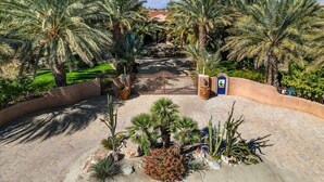 A landscaped area with palm trees, a paved walkway, and a gate leading to a building. - HUGE LUX Estate, Pool/Spa, Pickleball, Sleeps 22!
Date Grove Near Palm Springs (Thousand Palms)